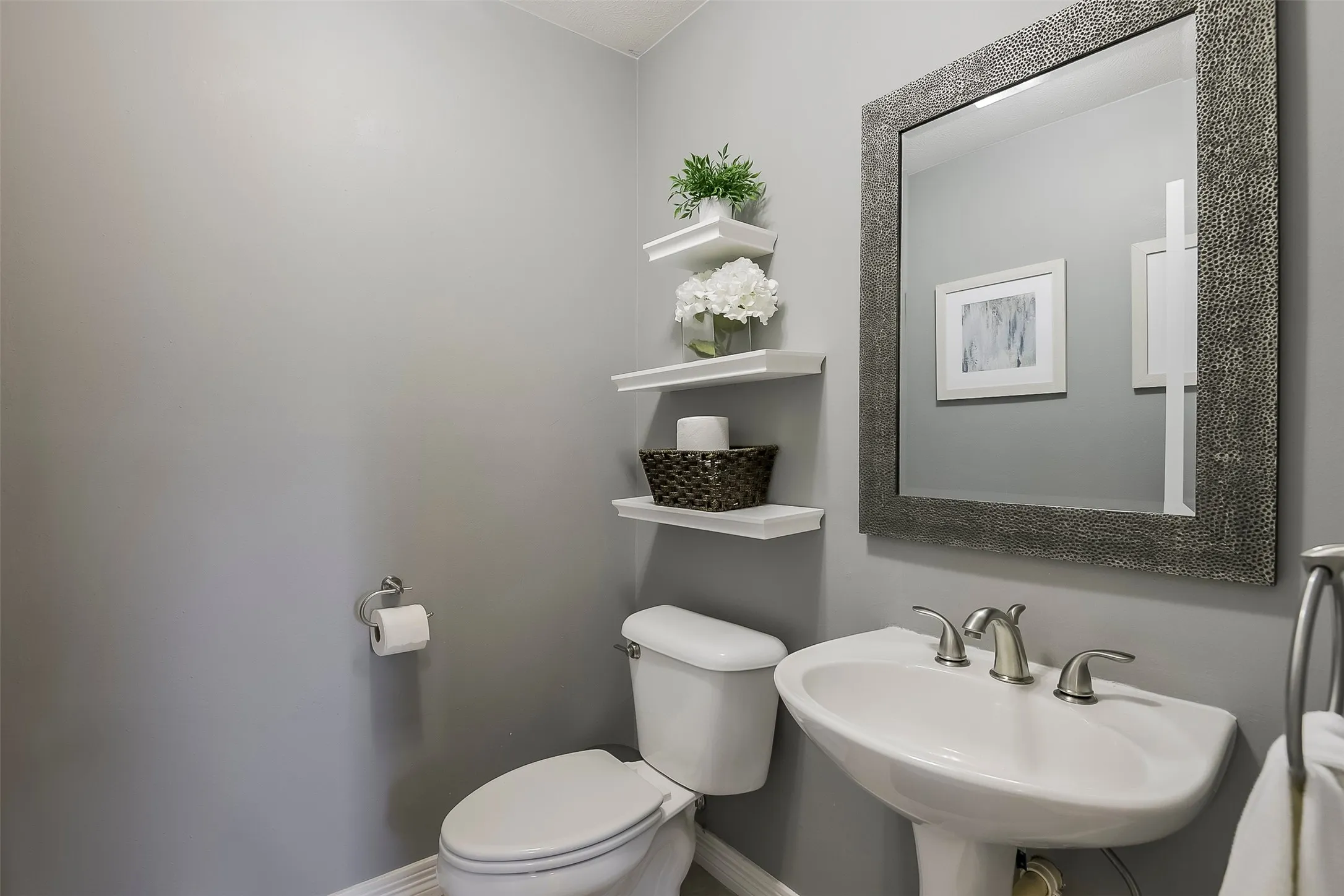 Pedestal sink with a brushed nickel faucet, framed mirror, and floating wall shelves