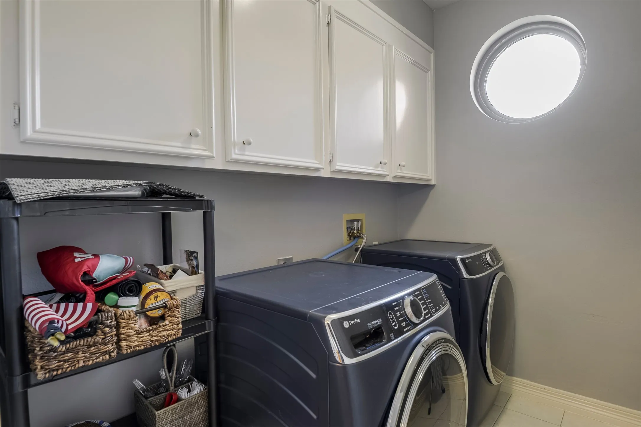 White upper cabinetry with decorative paneling, a circular window, and light tile flooring