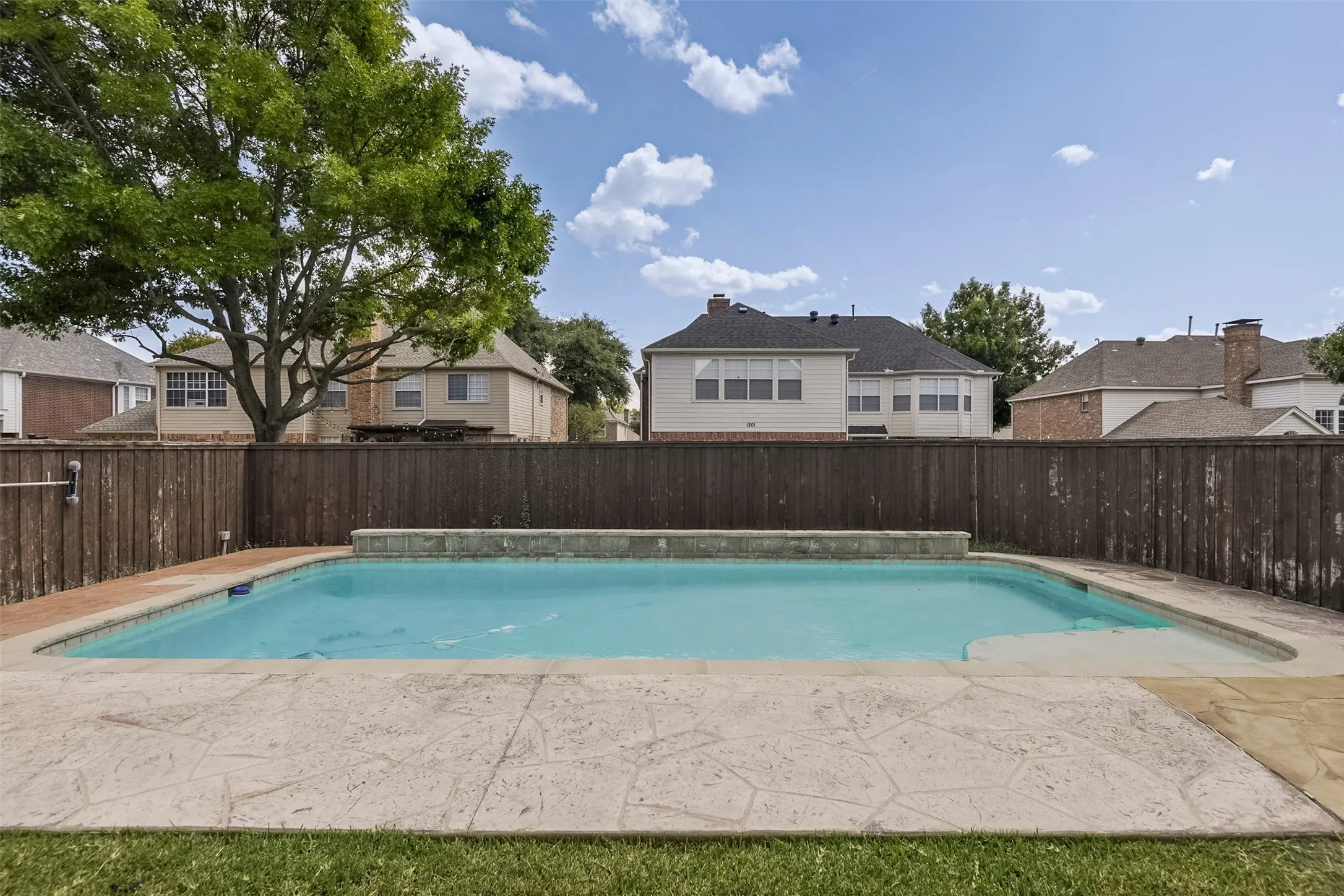 Rectangular inground pool with stamped concrete surround, stone coping, and a privacy fence
