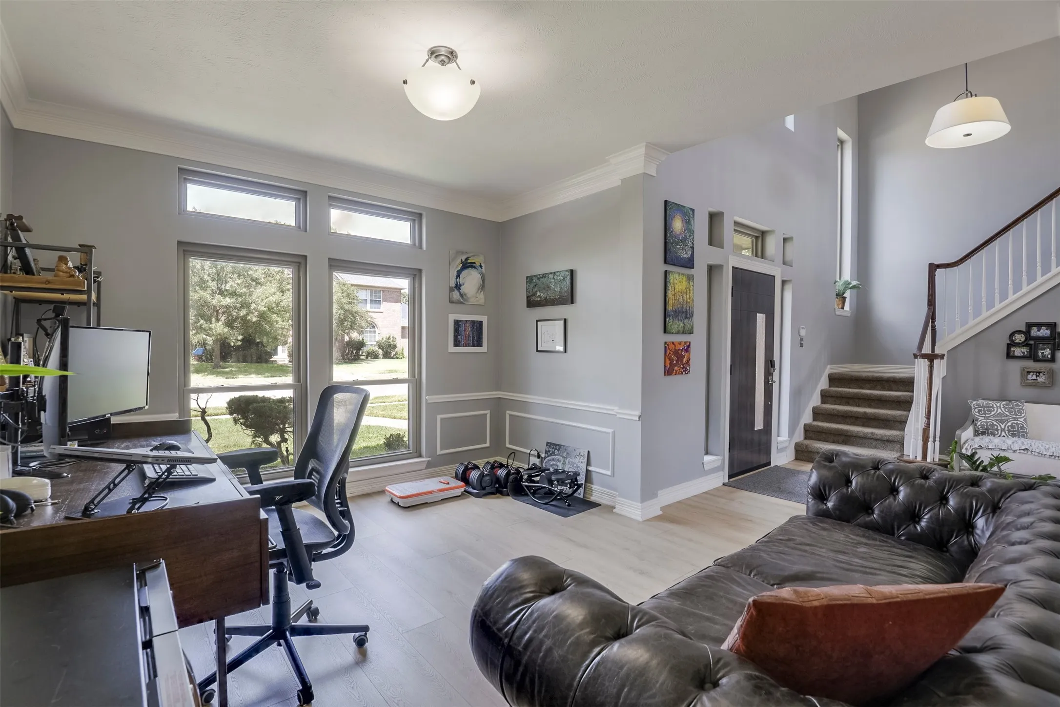 Spacious open-concept interior with wood-finish flooring, large windows, and crown molding
