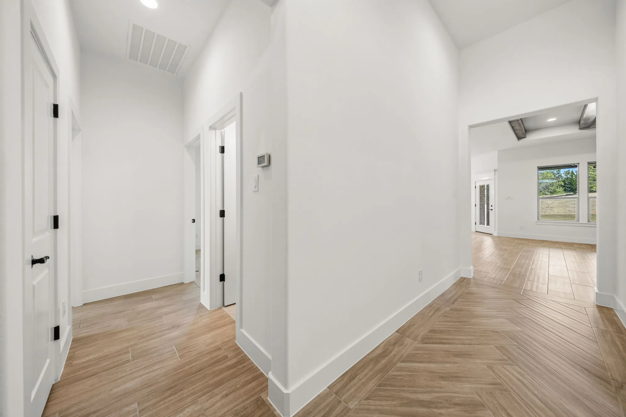 Hallway with wood-finish tile flooring in a herringbone pattern, clean white walls, and matte black door hardware