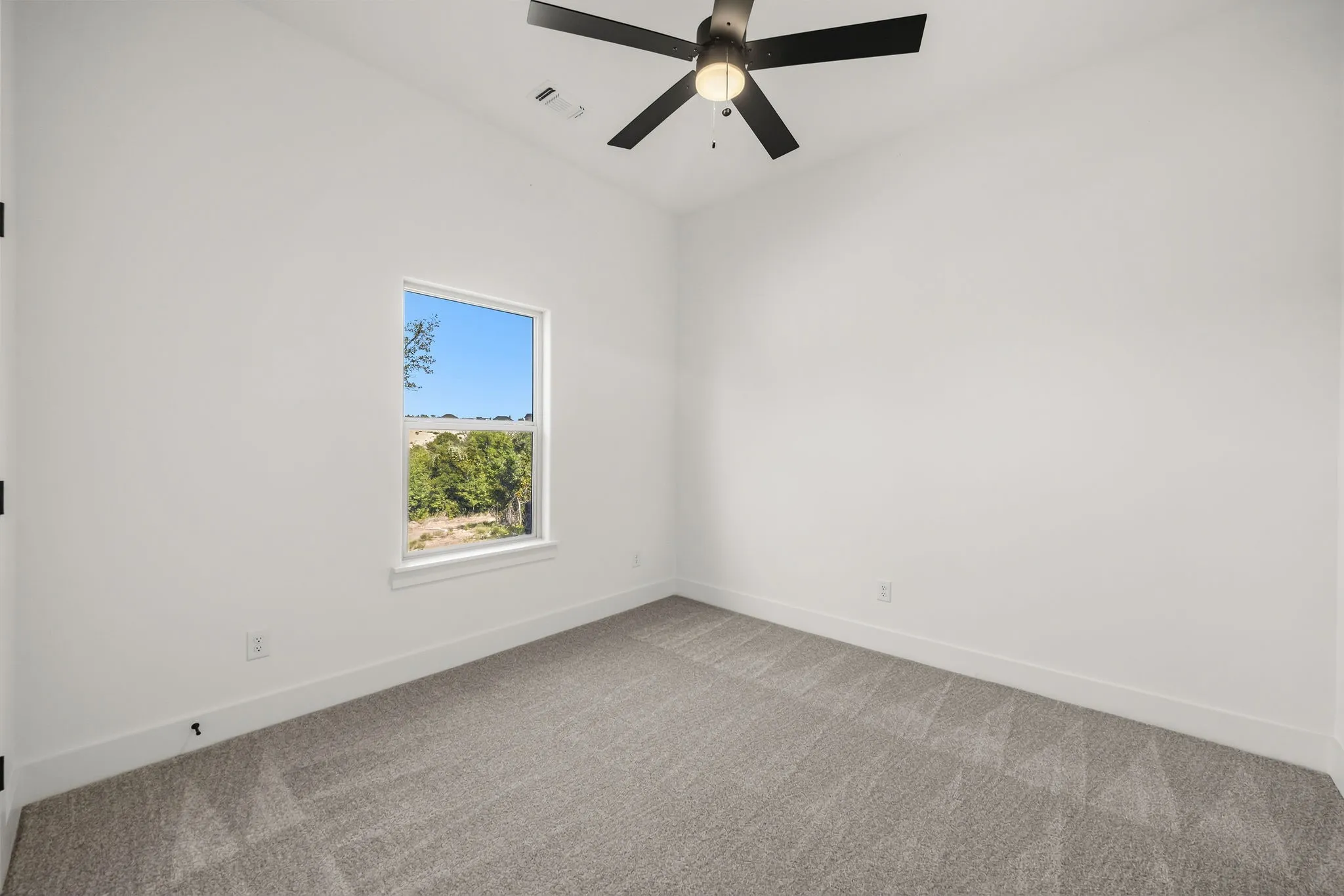 White walls with a single window, a ceiling fan, and gray patterned carpet