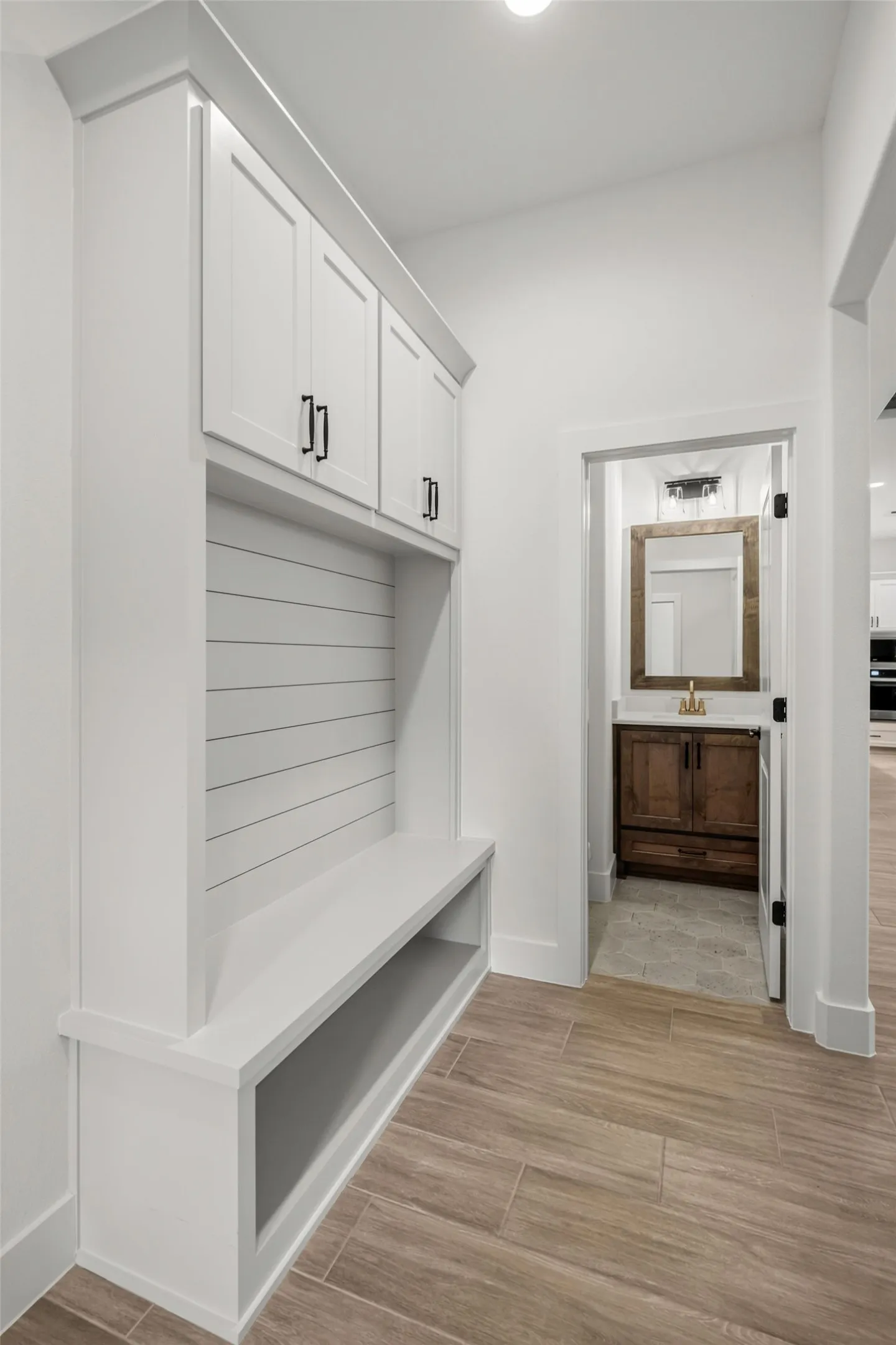 Built-in storage bench with overhead cabinetry and shiplap backing