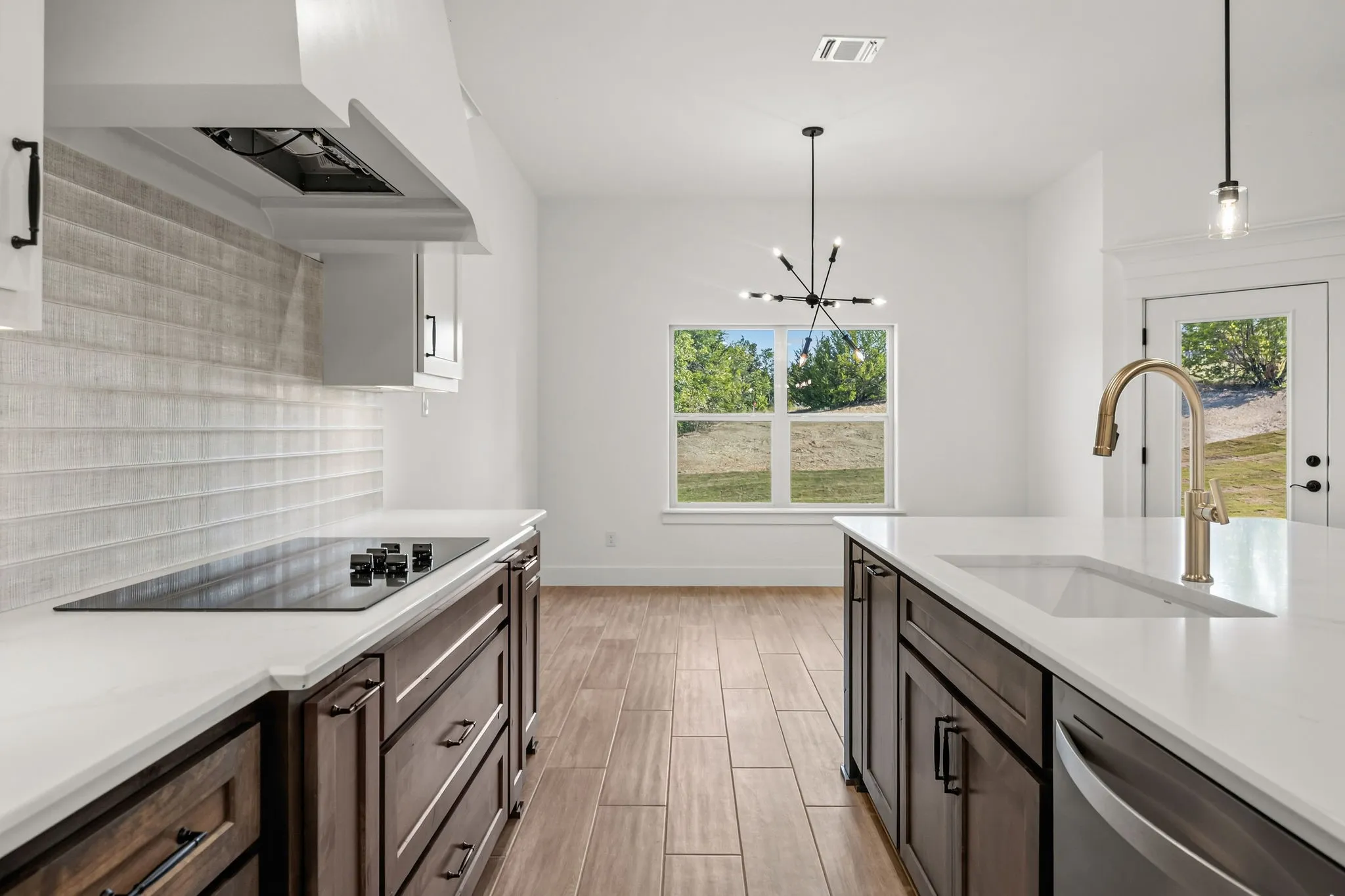 Spacious kitchen featuring dark wood-finish cabinetry, light countertops, an integrated cooktop, a large sink with a gooseneck faucet, and wood-finish flooring