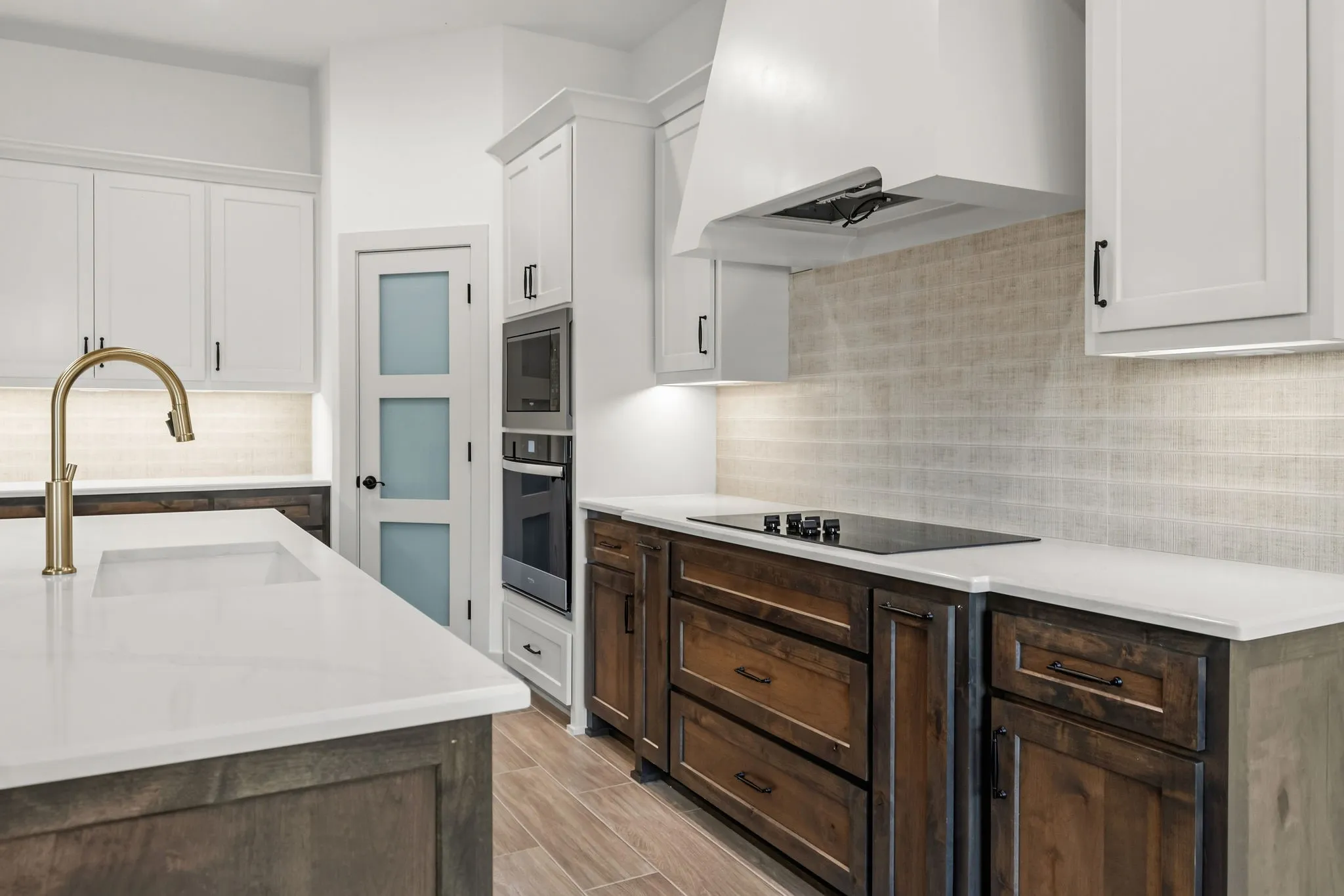 Kitchen featuring a brass-finish gooseneck faucet, integrated cooktop, built-in wall oven, microwave, and a pantry door with frosted glass panels