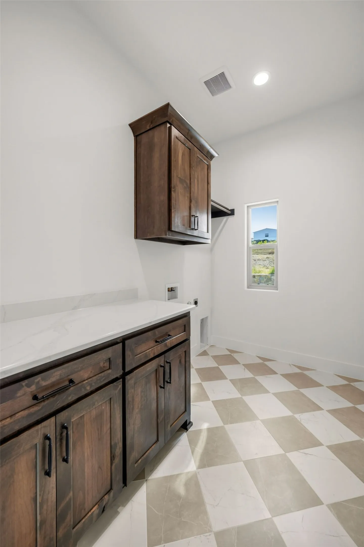 Laundry area featuring dark wood-finish cabinetry, white countertop, checkerboard floor tile, and a window