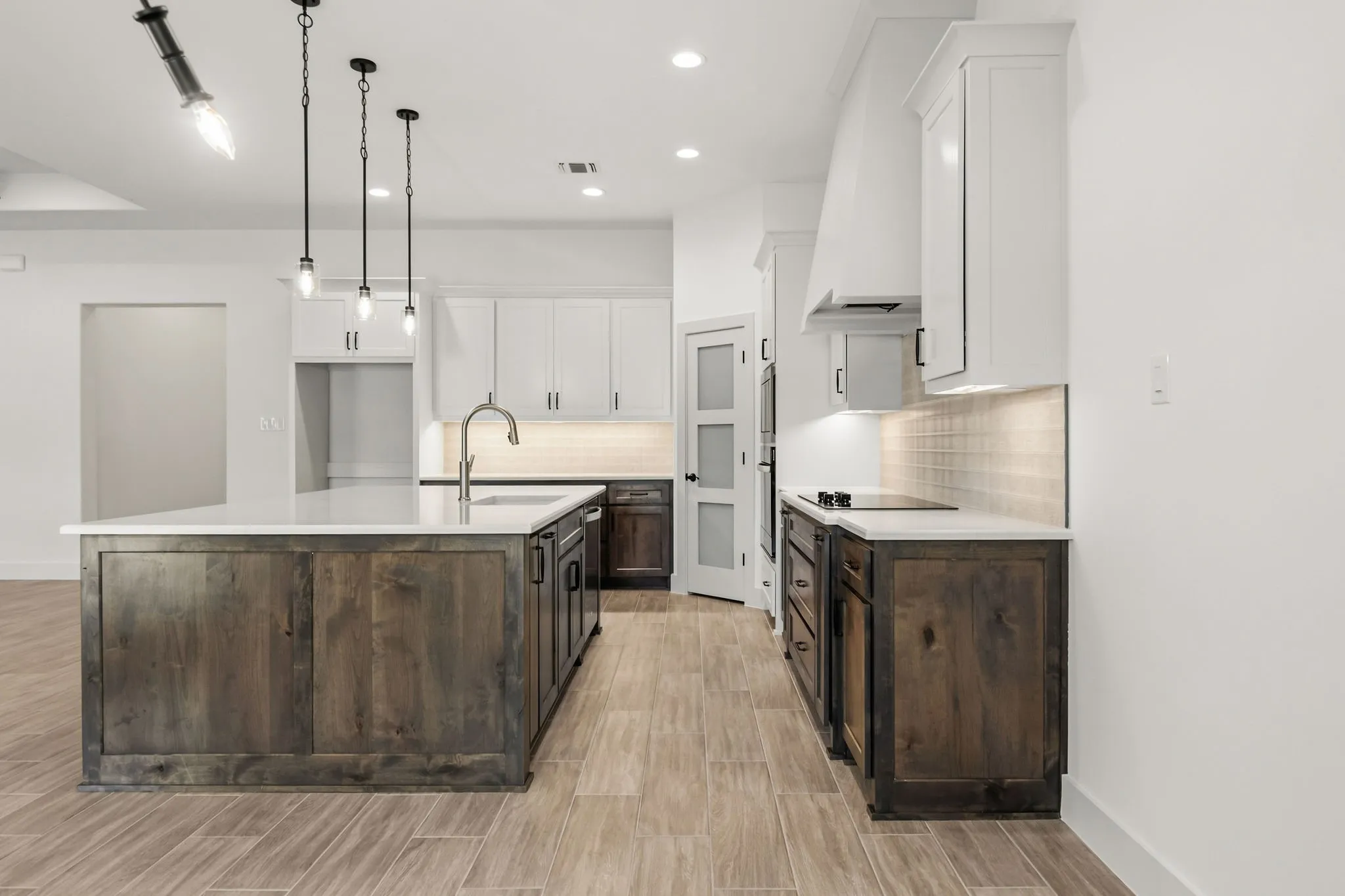 Kitchen featuring a large island with sink, pendant lighting, built-in cooktop, and contrasting cabinetry