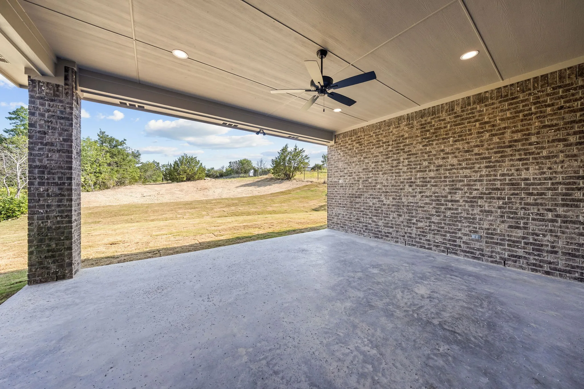 Covered concrete patio featuring a ceiling fan, recessed lighting, and a brick exterior wall