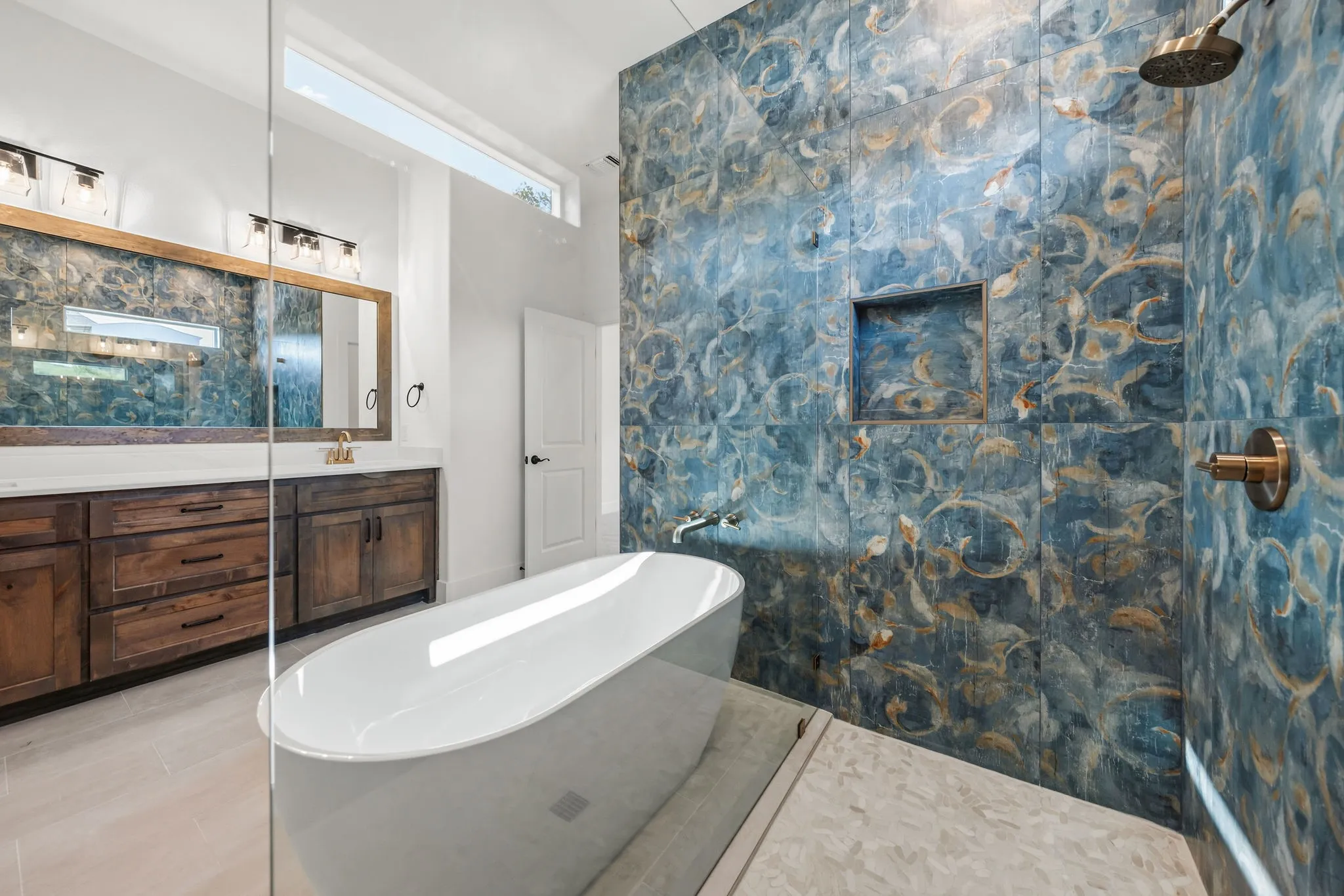 Spacious bathroom with a walk-in shower featuring decorative blue wall tile and a built-in shower niche