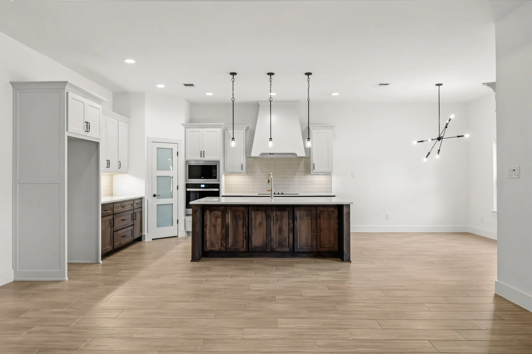 Open-concept kitchen featuring an island with a light-colored countertop, white upper cabinetry, built-in oven, and wood-finish flooring