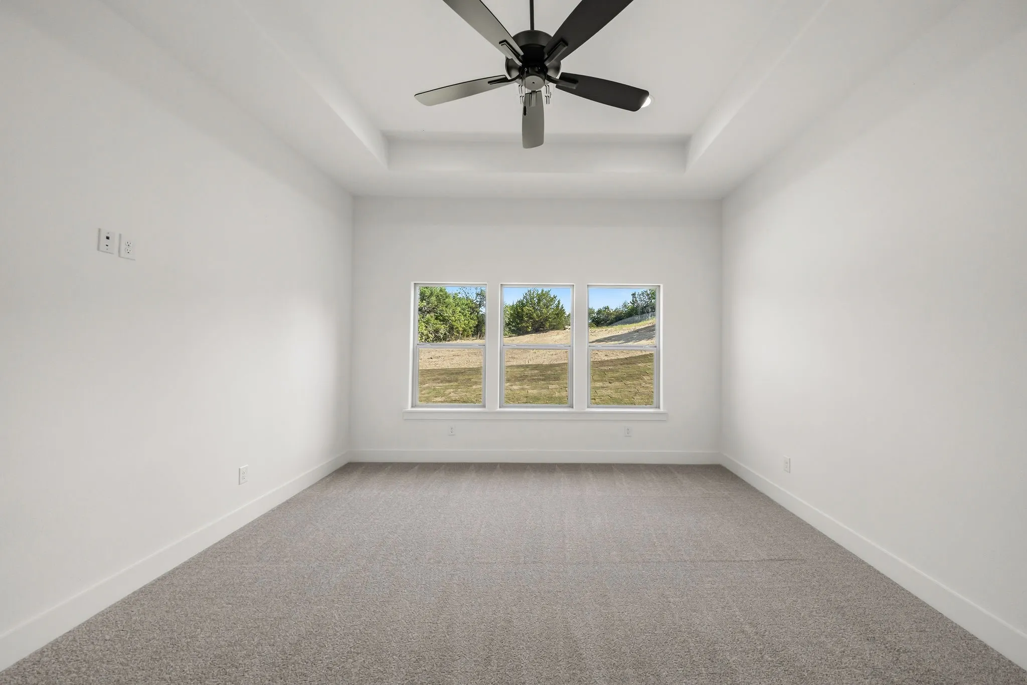 Tray ceiling with a black ceiling fan, three horizontal windows, and gray carpeting
