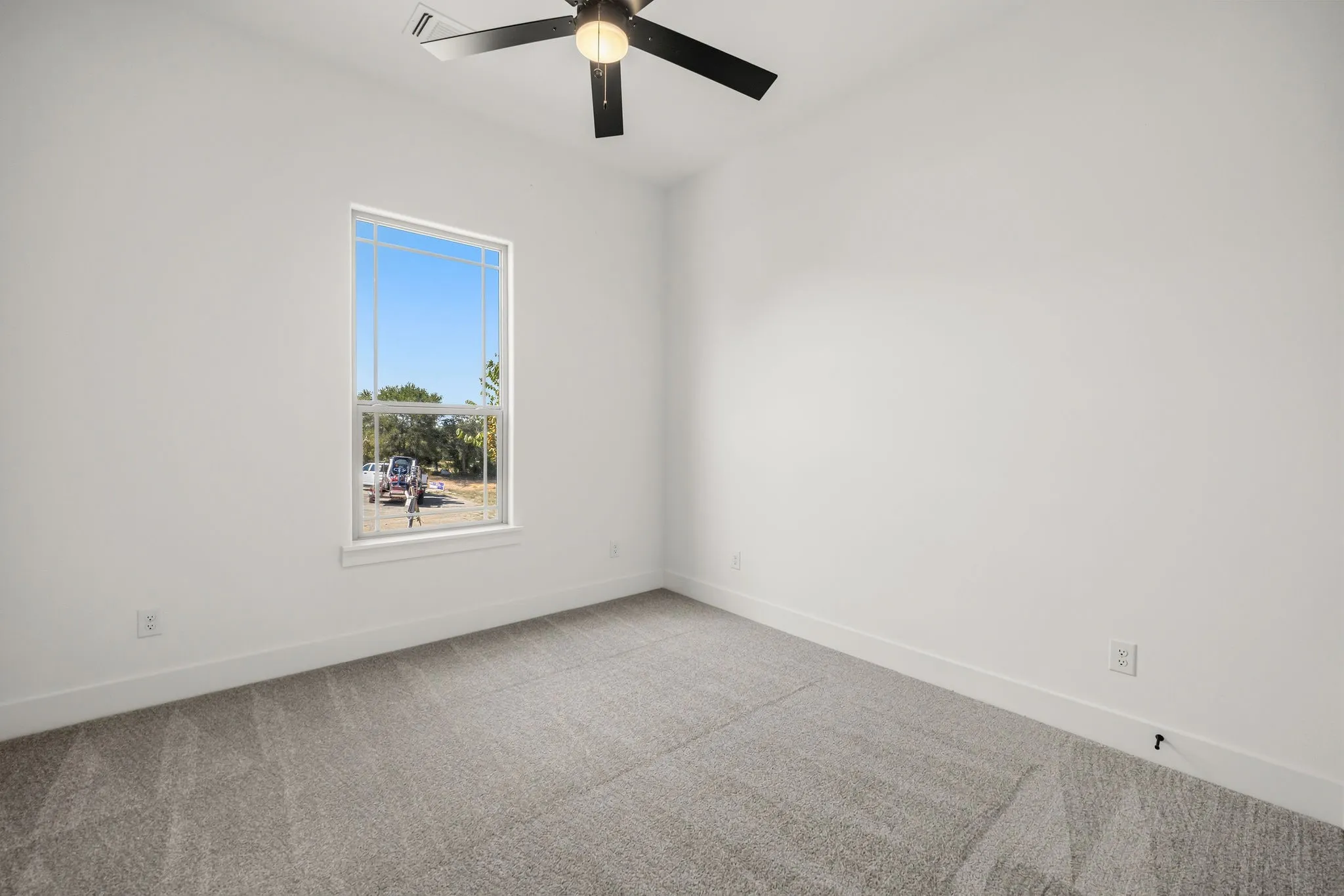 Neutral-toned walls and carpeting, ceiling fan with light fixture, and natural light from a double-hung window