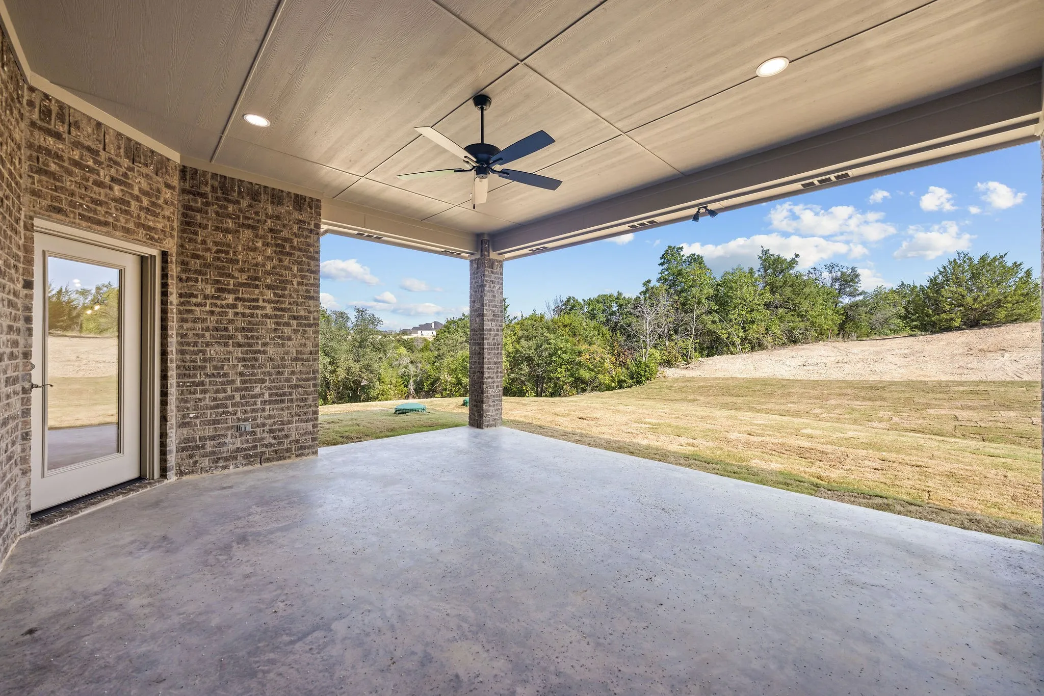 Covered patio featuring a ceiling fan, recessed lighting, brick exterior walls, and a glass-paneled door