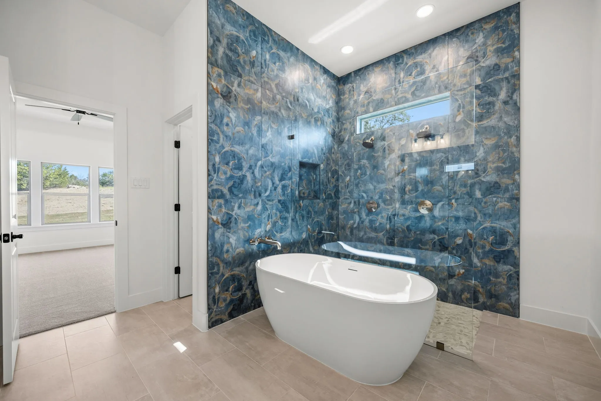 Freestanding soaking tub with a tiled accent wall, glass-enclosed shower, and a transom window