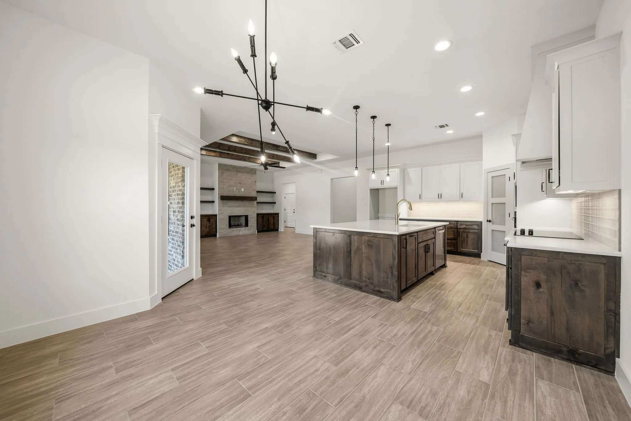 Open-concept living space with wood-finish flooring, a kitchen island with stone countertop, and an exposed beam ceiling