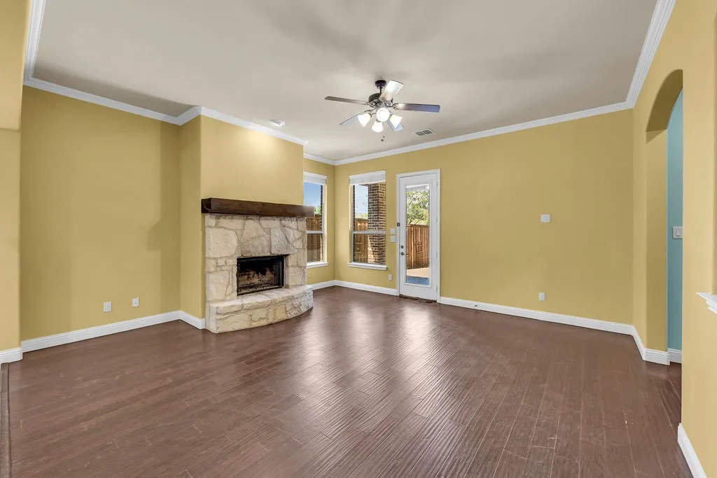 Spacious interior featuring wood-finish flooring, a stone fireplace with a wood mantle, multiple windows, and a ceiling fan
