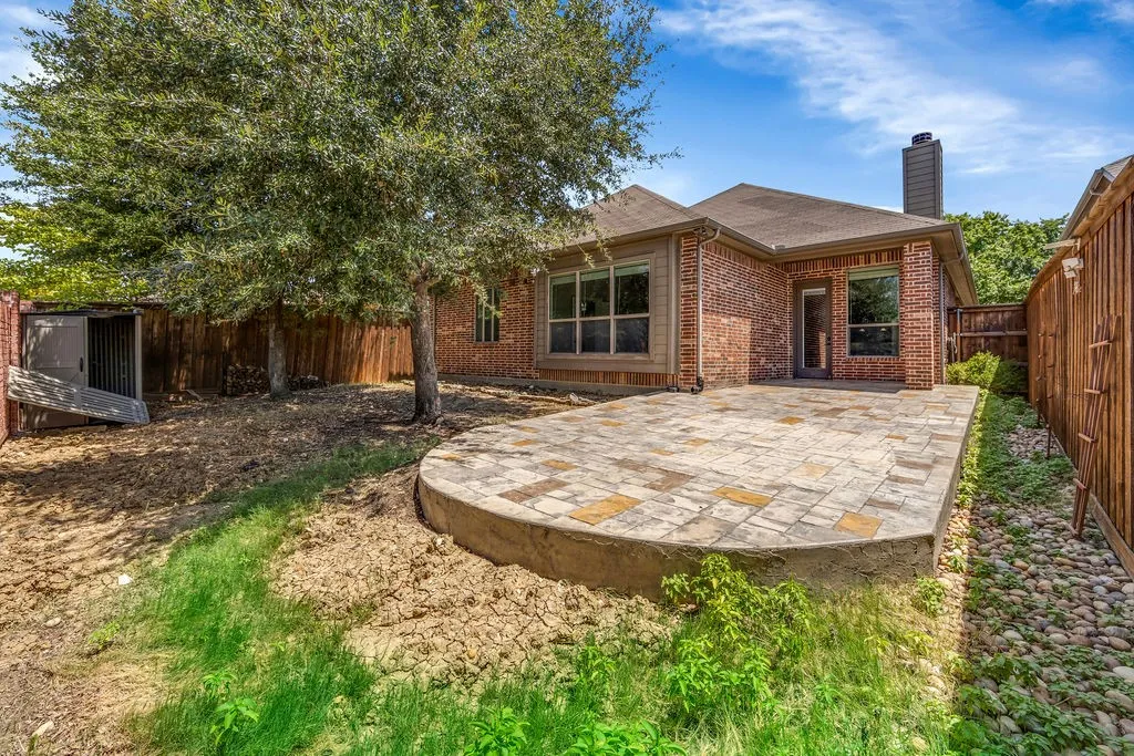 Brick exterior construction featuring an elevated patio with paver stone flooring, a mature tree, and a wood privacy fence