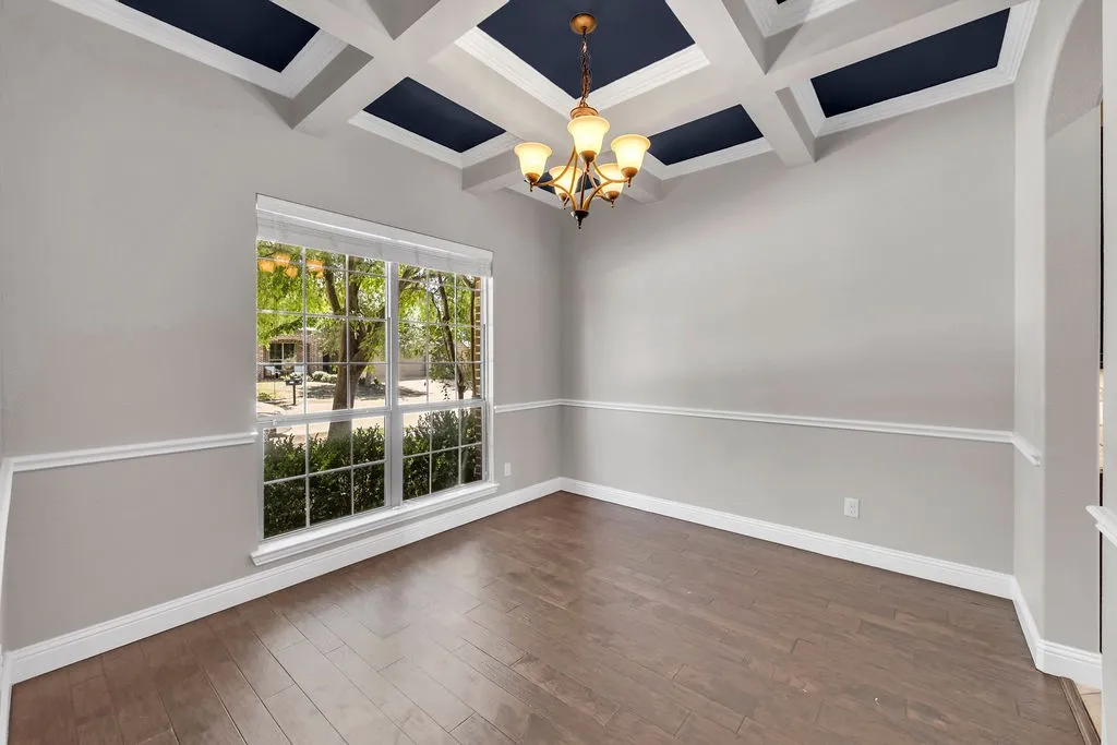 Coffered ceiling with accent panels, elegant chandelier, large picture window, chair rail molding, and wood-finish flooring