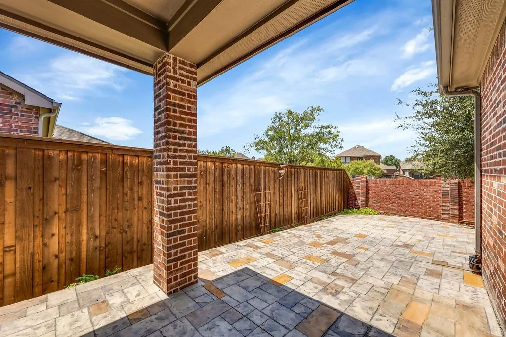 Covered patio with brick column, decorative paved flooring, wood privacy fencing, and a partial brick privacy wall