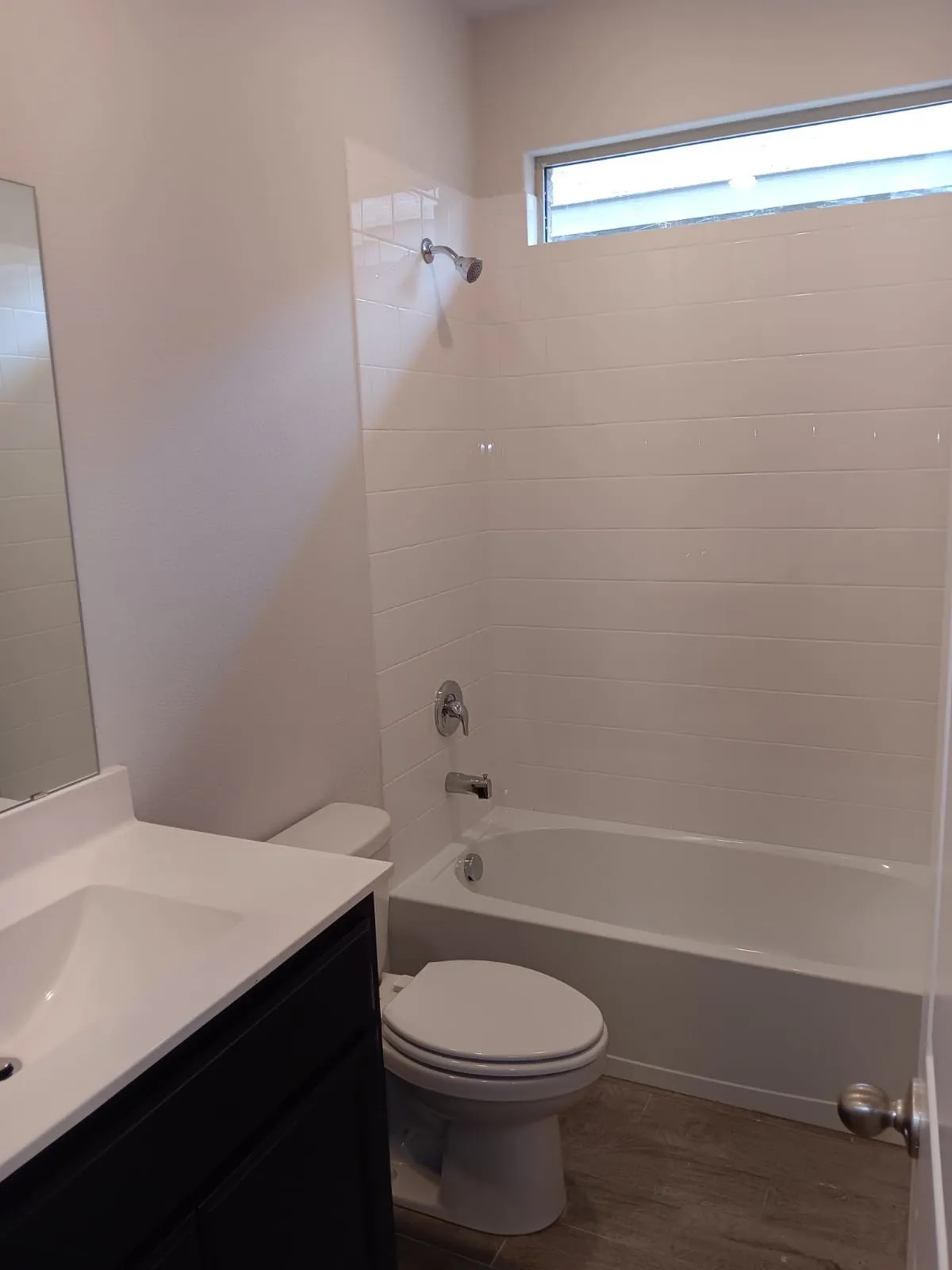 Bathroom featuring a shower/tub combination with white subway tile surround, white vanity with integrated sink, dark wood-finish vanity cabinetry, and wood-finish flooring