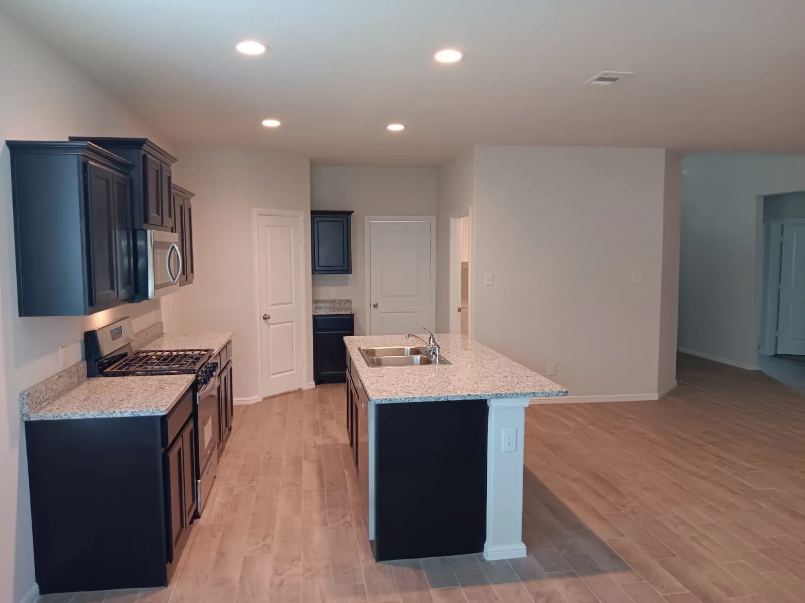 Kitchen featuring dark wood cabinetry, granite countertops, a stainless steel gas range, and an island with an integrated sink