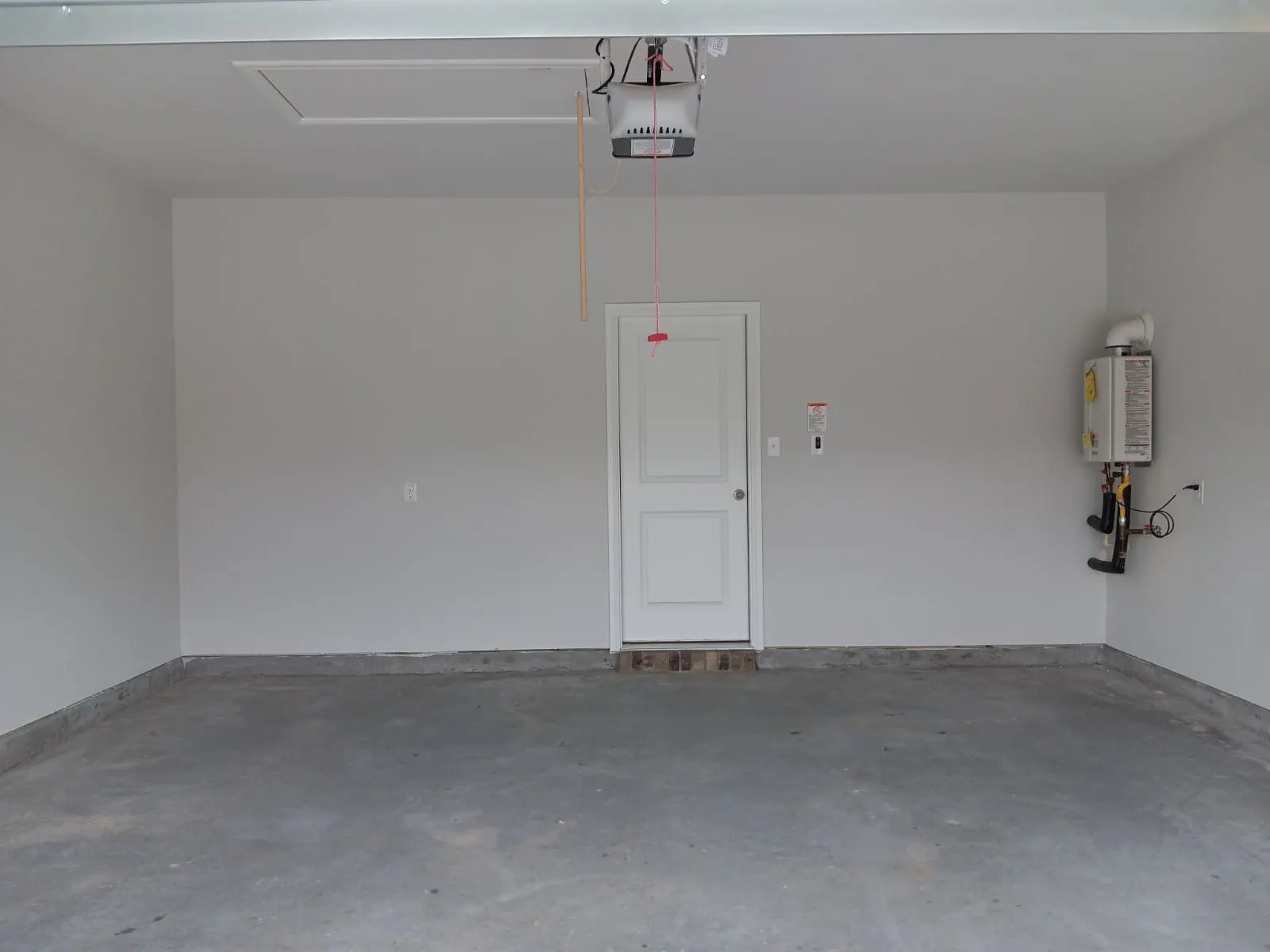 Attached single-panel door, concrete flooring, overhead garage door mechanism, ceiling access panel, and wall-mounted water heater