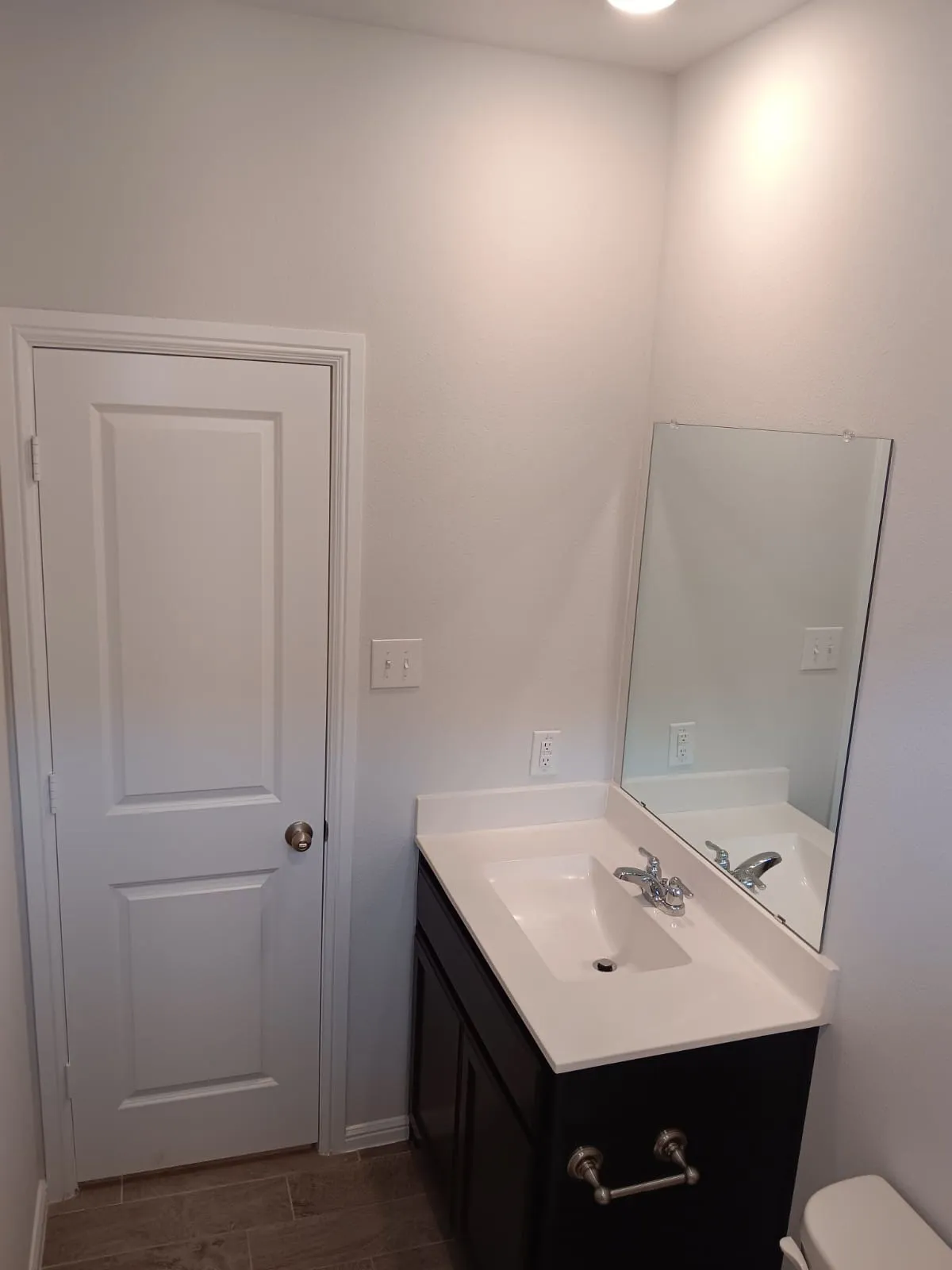 White paneled door, wood-finish flooring, dark wood vanity with white countertop, integrated sink, and wall-mounted mirror