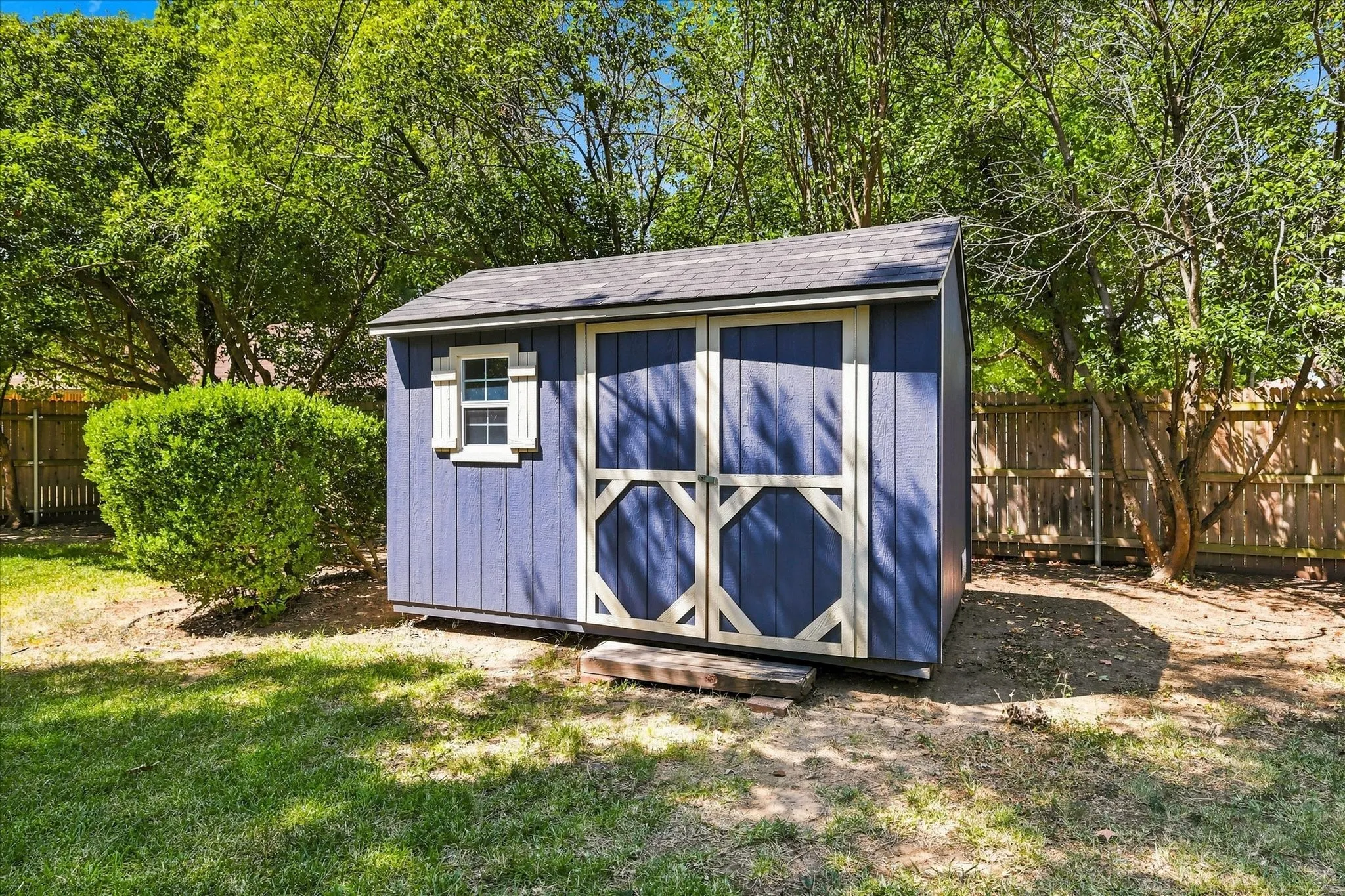 Expansive backyard featuring a stone fire pit, natural stone stepping stones, a wooden privacy fence, mature trees, and a storage shed