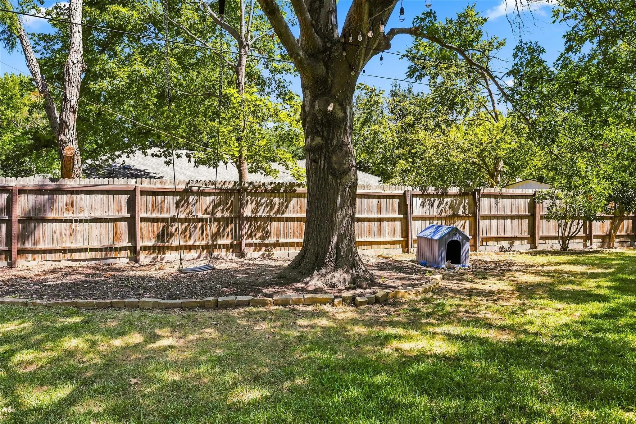 Expansive backyard featuring a stone fire pit, natural stone stepping stones, a wooden privacy fence, mature trees, and a storage shed