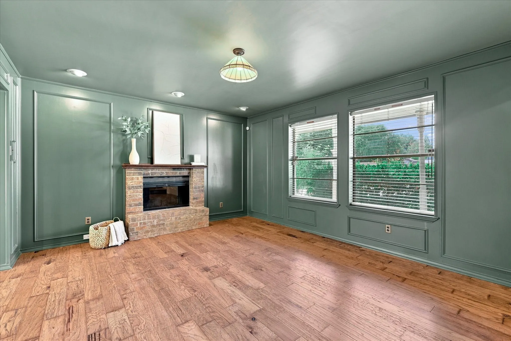 The living room features beautiful wood floors and on-trend color-drenched paint. A brick wood-burning fireplace features a raised hearth and wood mantel.  Lots of natural light fills this cozy room from the front windows.