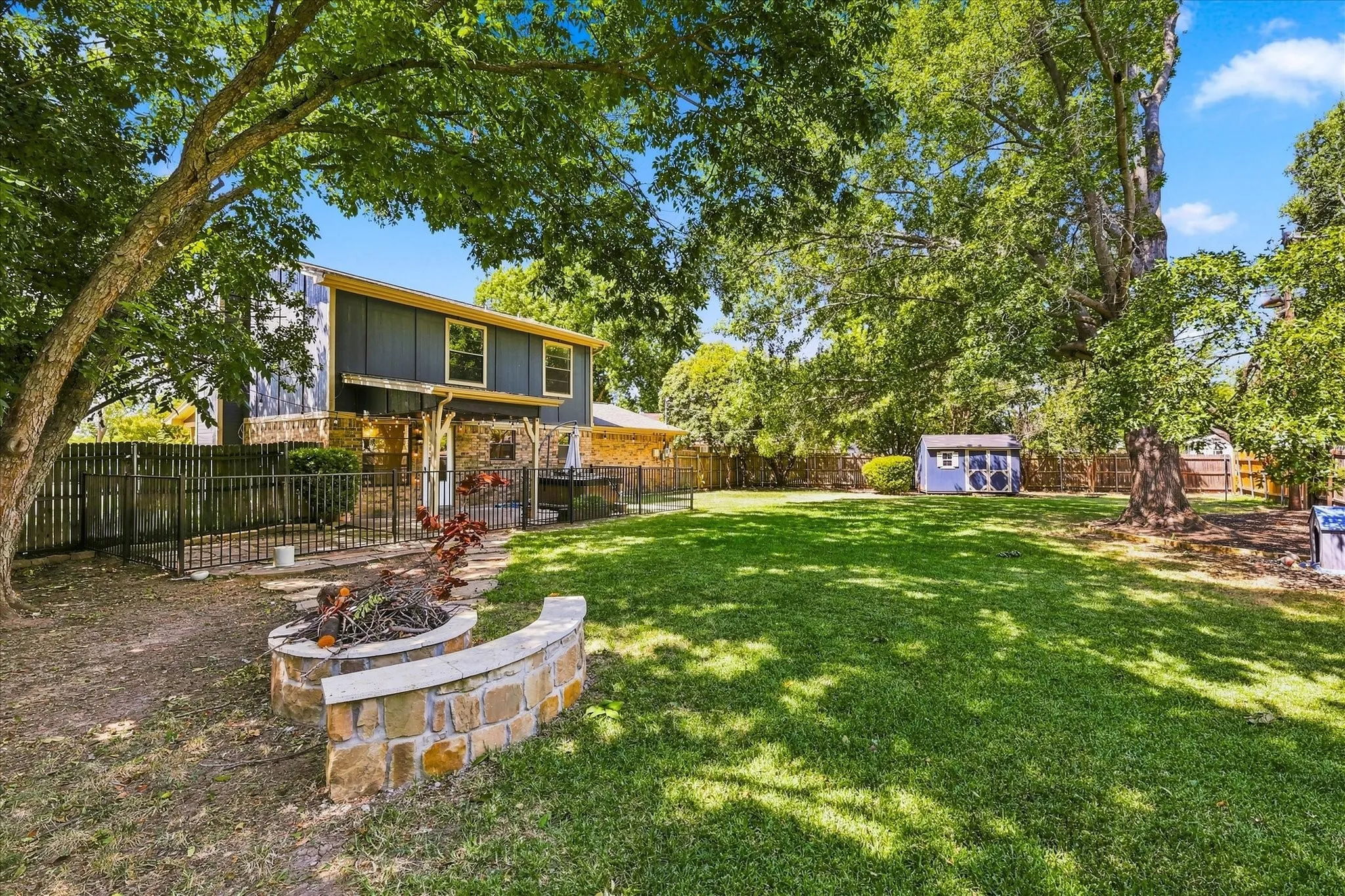 Expansive backyard featuring a stone fire pit, natural stone stepping stones, a wooden privacy fence, mature trees, and a storage shed