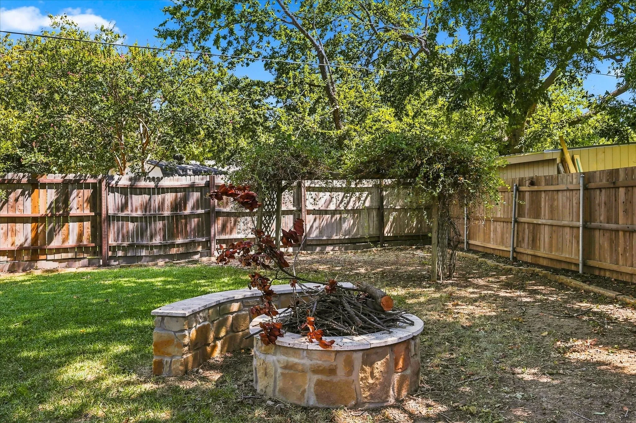 Expansive backyard featuring a stone fire pit, natural stone stepping stones, a wooden privacy fence, mature trees, and a storage shed