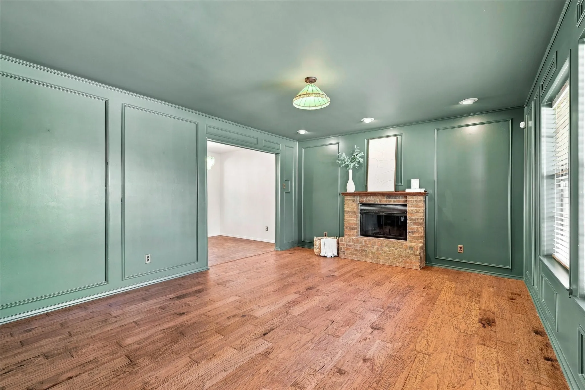 The living room features beautiful wood floors and on-trend color-drenched paint. A brick wood-burning fireplace features a raised hearth and wood mantel.  Lots of natural light fills this cozy room from the front windows.