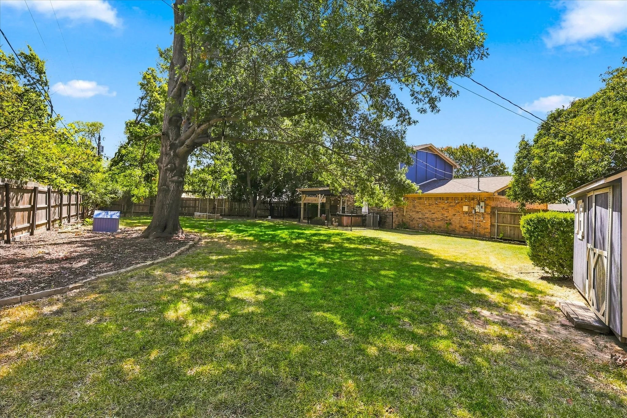Expansive backyard featuring a stone fire pit, natural stone stepping stones, a wooden privacy fence, mature trees, and a storage shed