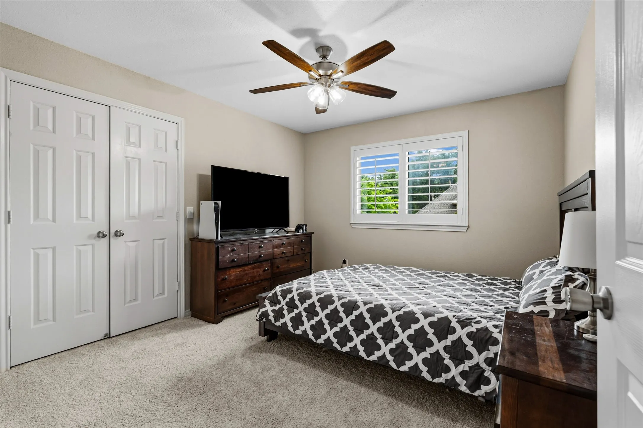 Plush carpet flooring, wood-finish ceiling fan, window with plantation shutters, and paneled closet doors