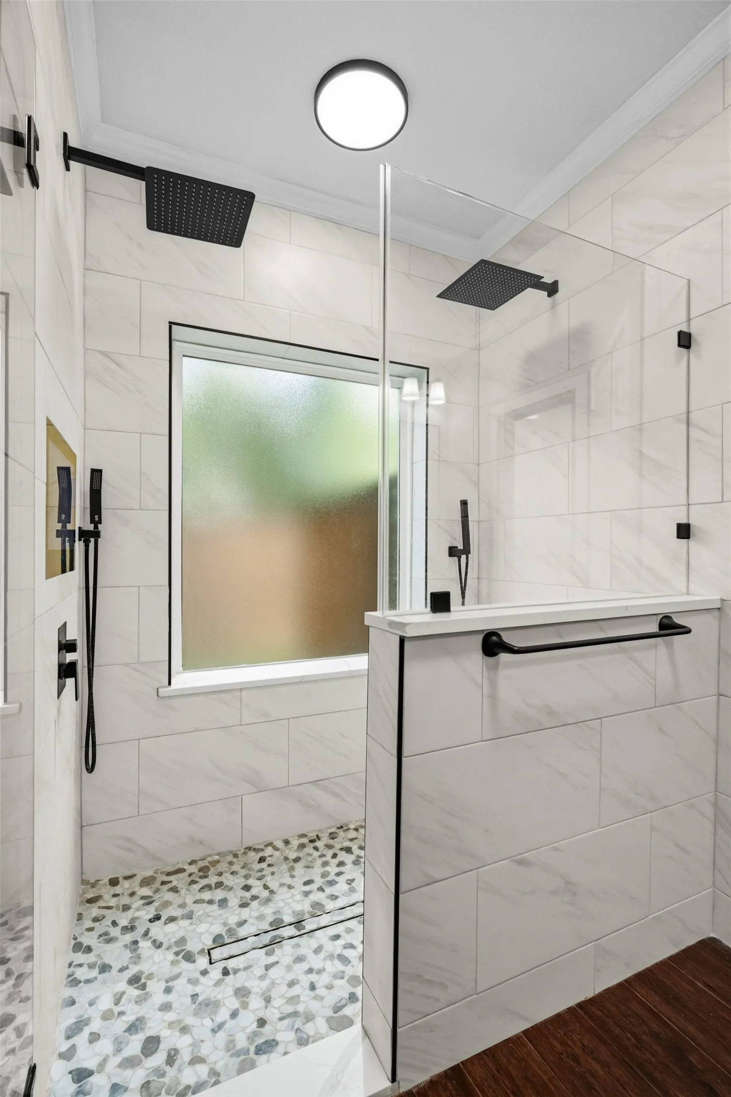 Walk-in shower with dual matte black rainfall shower heads, pebble-finish flooring, and white tile surround