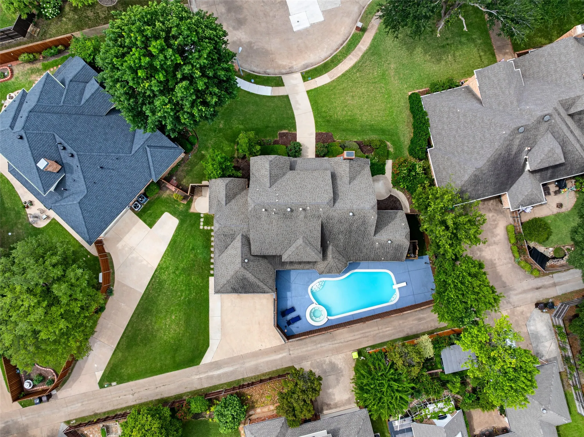 Curved swimming pool with an integrated spa, surrounded by a paved patio