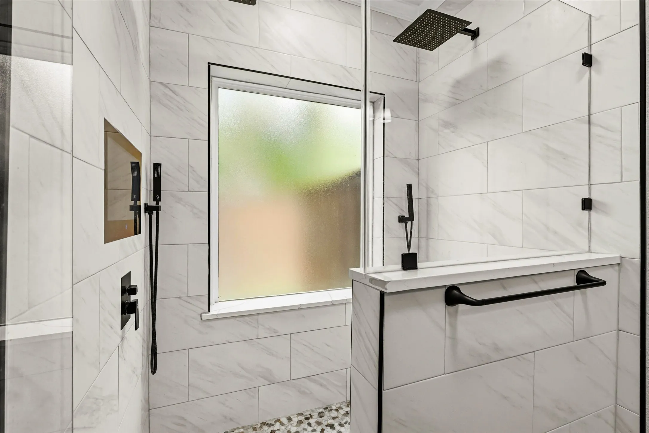 Tiled shower enclosure featuring a fixed glass panel, pebble floor, and matte black fixtures