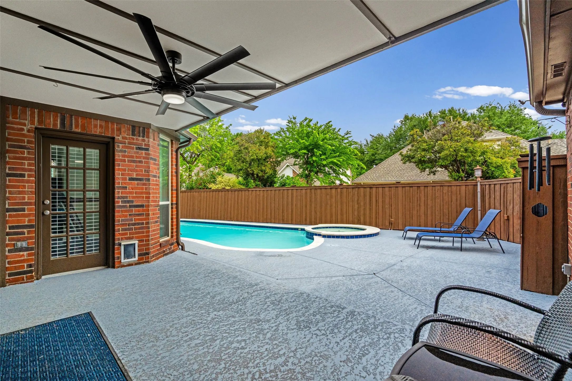 Covered patio with a multi-blade ceiling fan, brick exterior, and a glass-paneled door