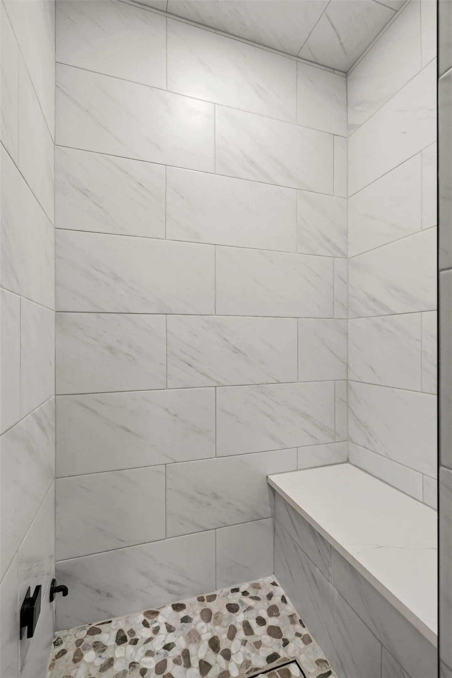 Steam room with large format subway tile, built-in bench, and pebble-tile flooring