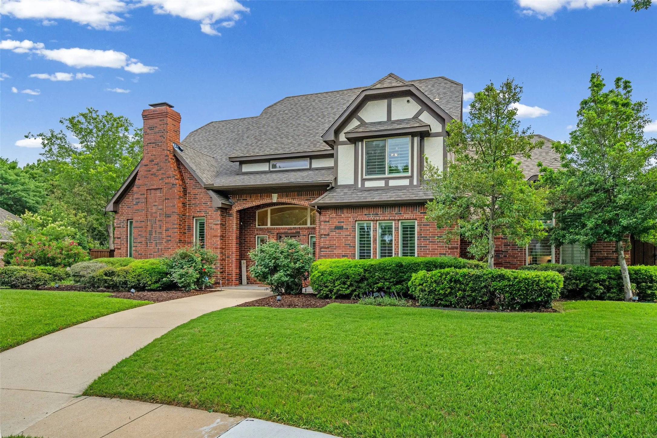 Brick exterior with a prominent chimney, Tudor-style accents, mature landscaping, and an arched entry