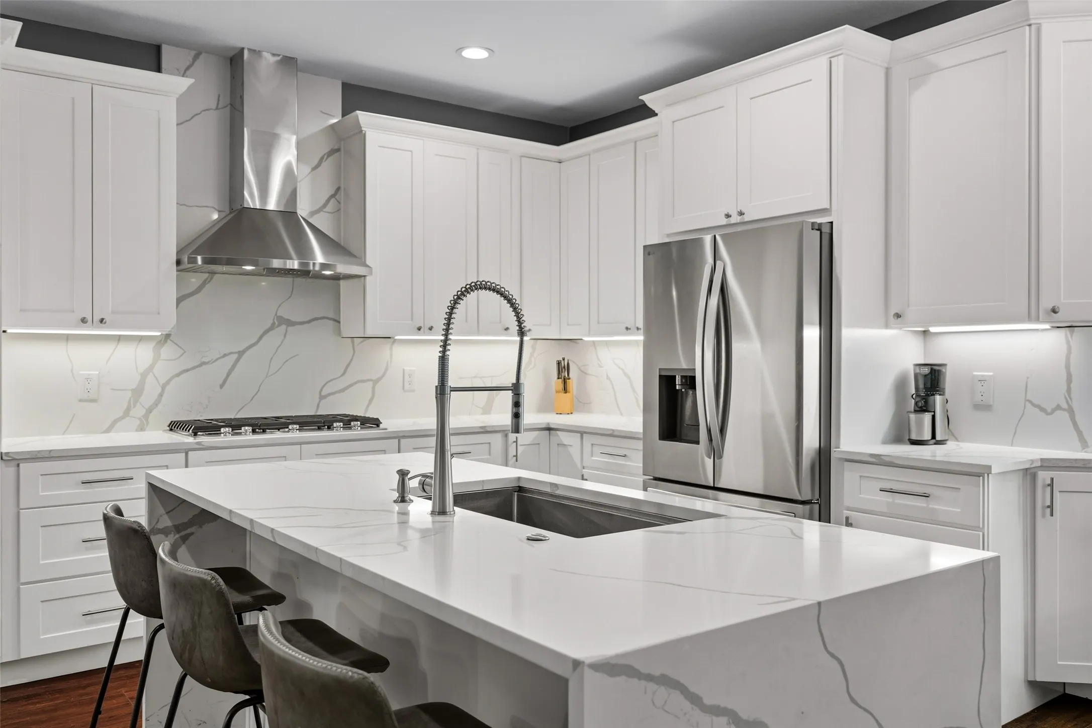 Full kitchen featuring white shaker cabinetry, stainless steel appliances, a large center island with an integrated sink, and stone countertops with a matching backsplash