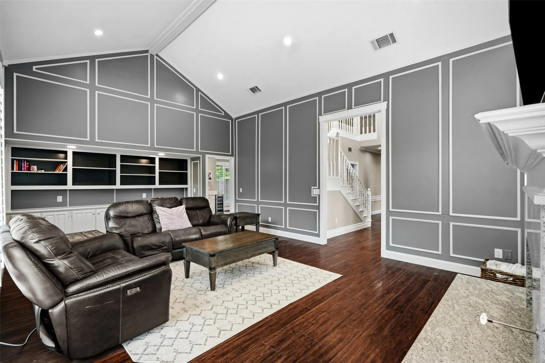 Vaulted ceiling, built-in shelving, wood-finish flooring, decorative wall molding, and a fireplace surround