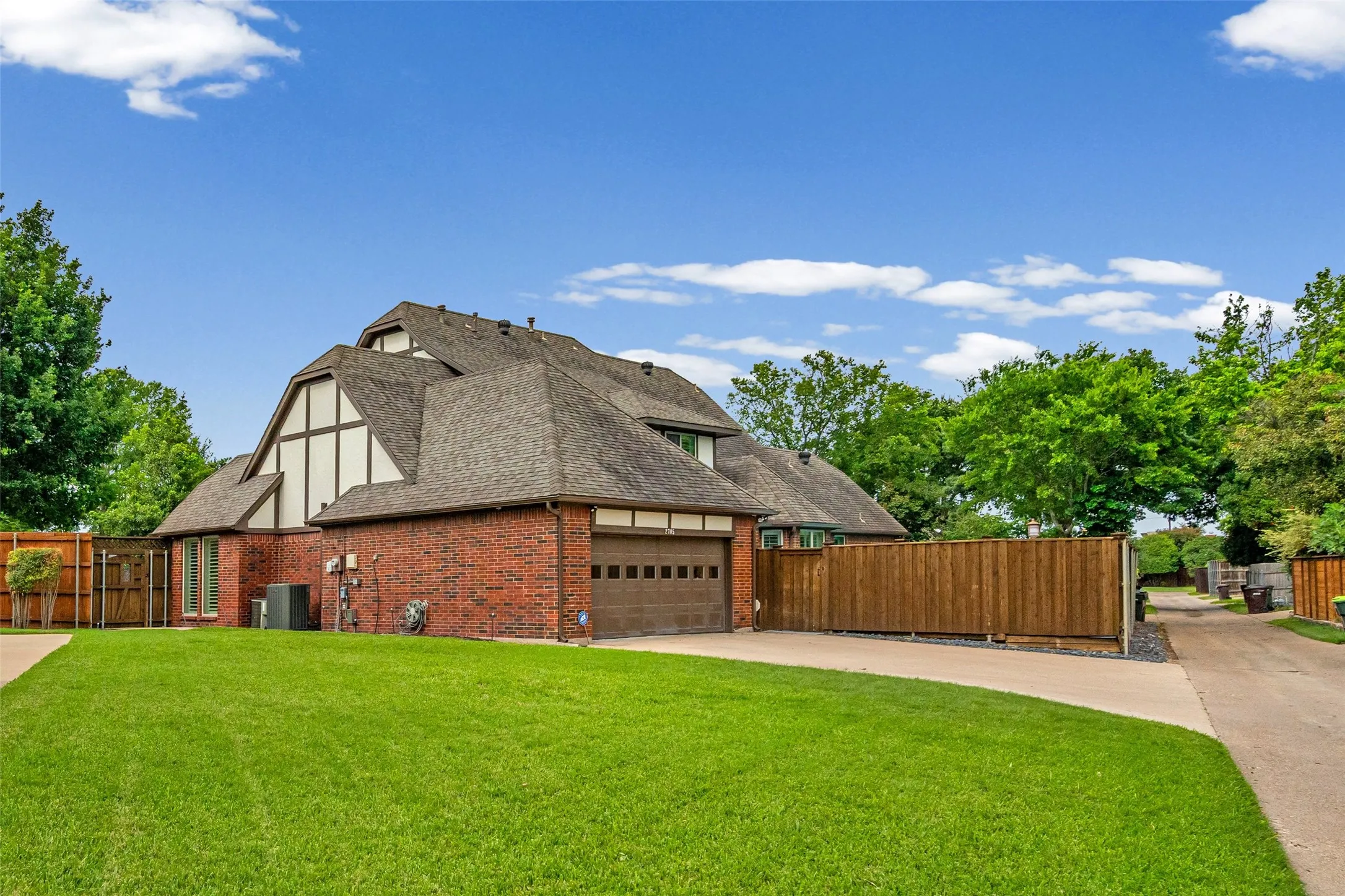 Brick exterior with a peaked roofline, attached garage, and a lush green lawn