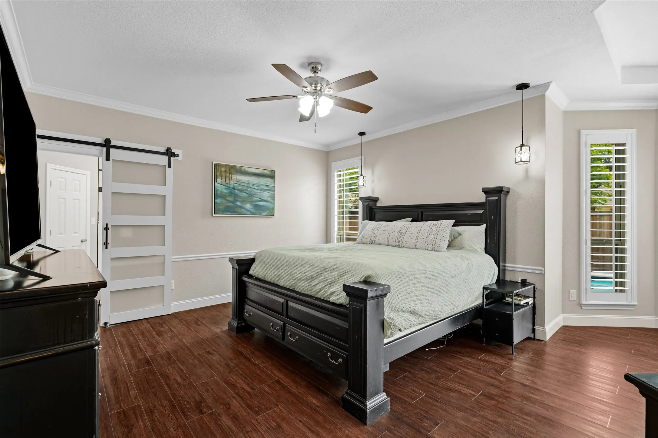 Wood-finish flooring, crown molding, ceiling fan, contemporary barn door, and suspended pendant lighting fixtures