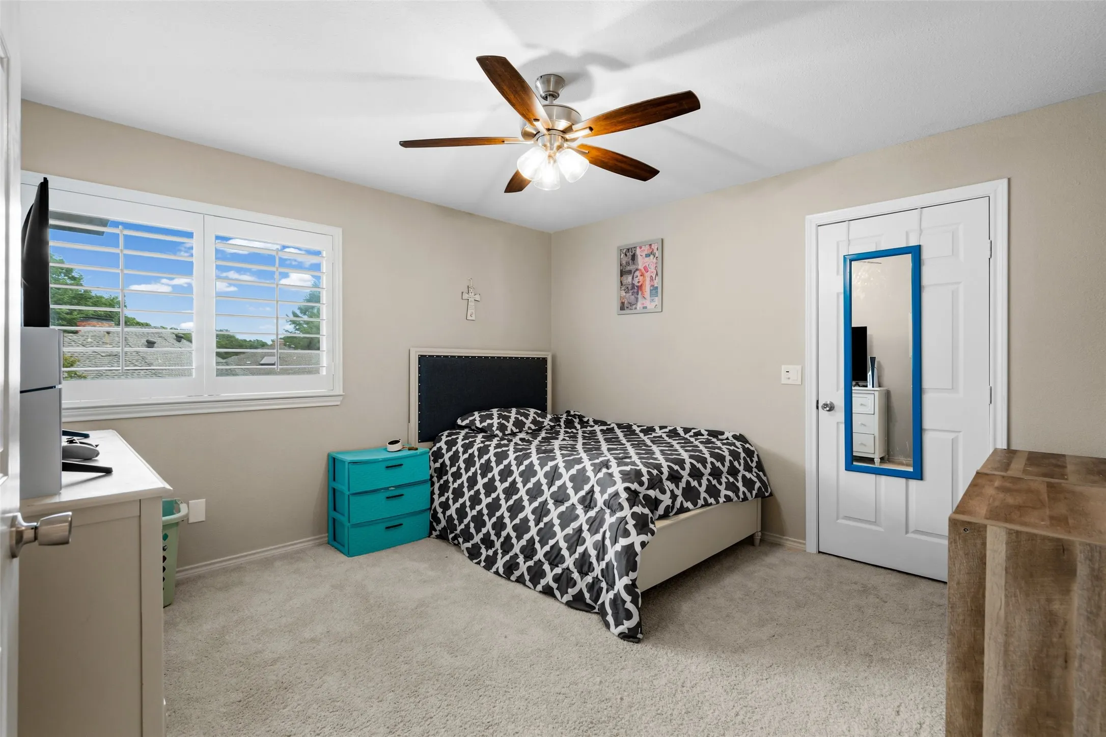 Carpeted room featuring a ceiling fan with light, a window with plantation shutters, and a white door