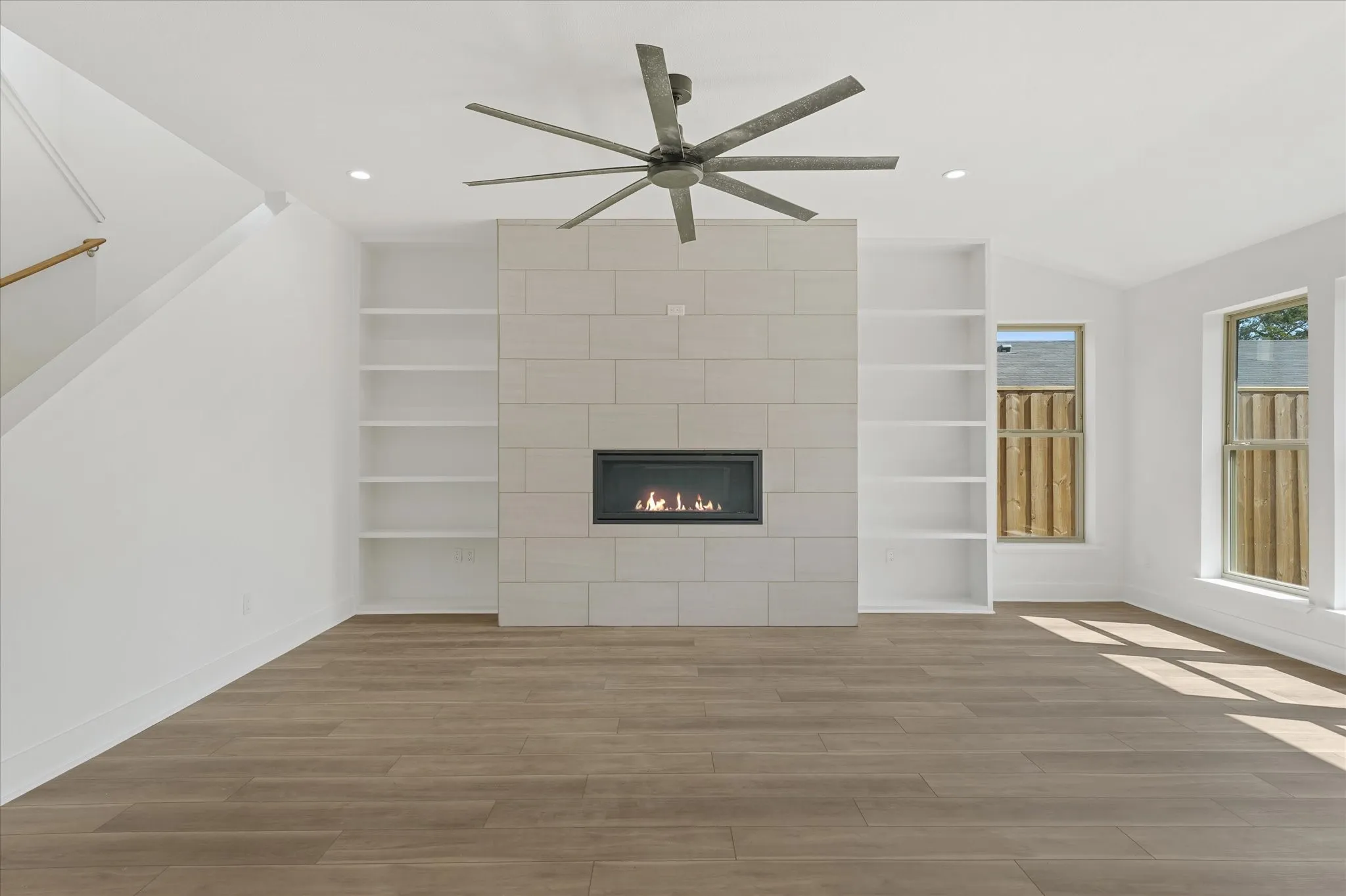 Recessed fireplace with a tile surround, built-in shelving, wood-finish flooring, and a ceiling fan