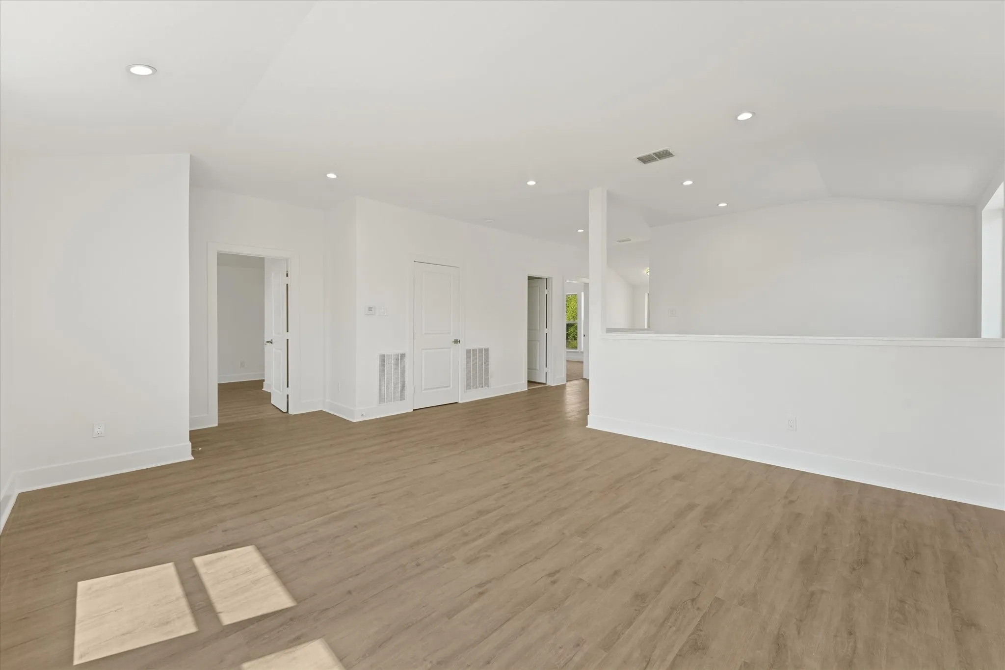 Light wood-finish flooring, three large windows, recessed lighting, and a built-in wood-finish bookcase