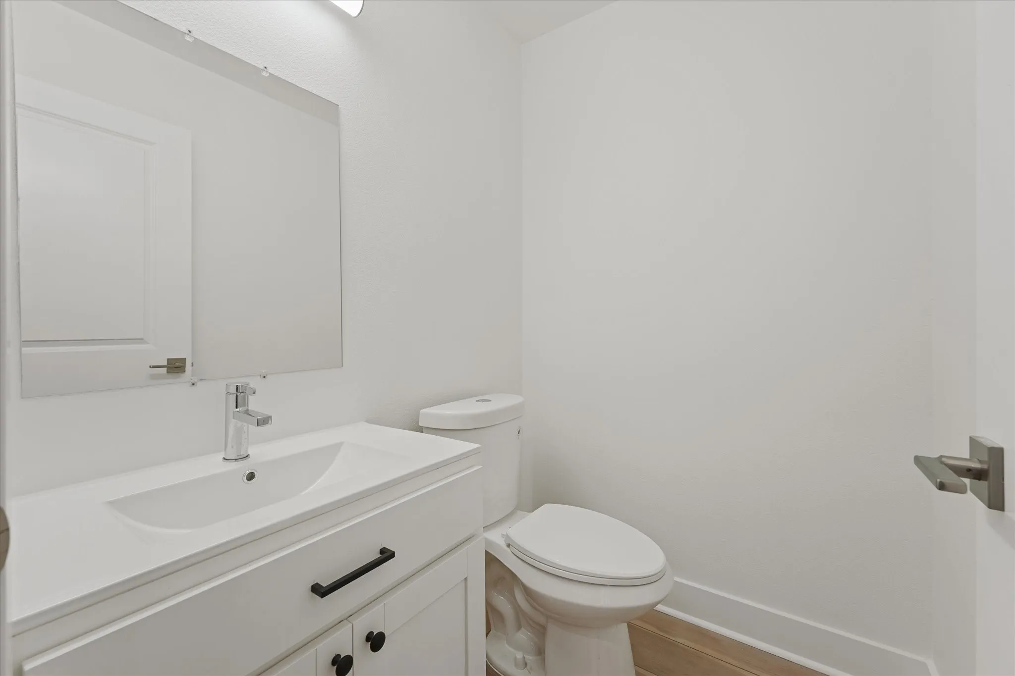 Contemporary bathroom featuring a white vanity with integrated sink, chrome faucet, wall-mounted mirror, and wood-finish flooring