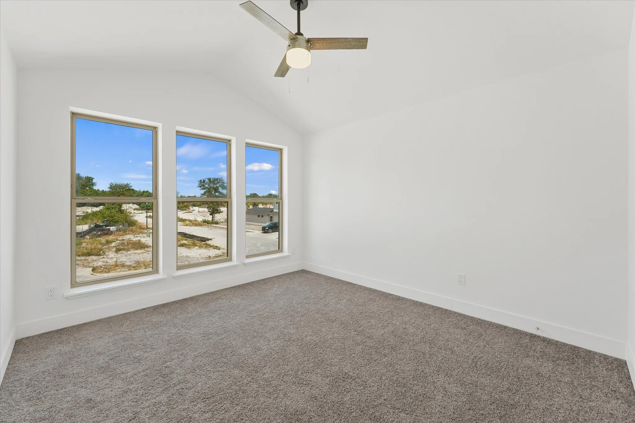 Vaulted ceiling with an attached ceiling fan, three large windows, gray carpet, and white walls